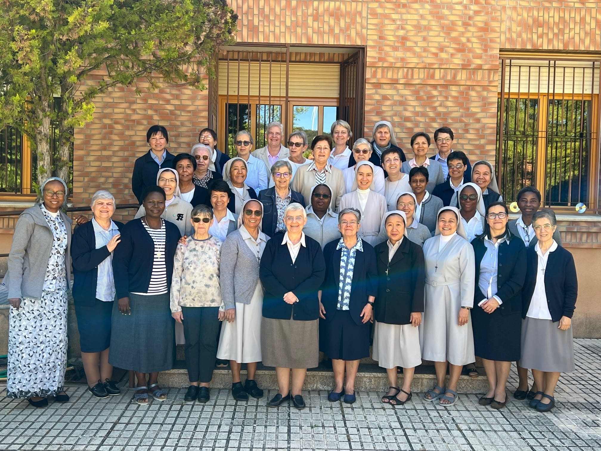 Gran grupo de Hermanas Hospitalarias posando juntas frente a un edificio de ladrillo.